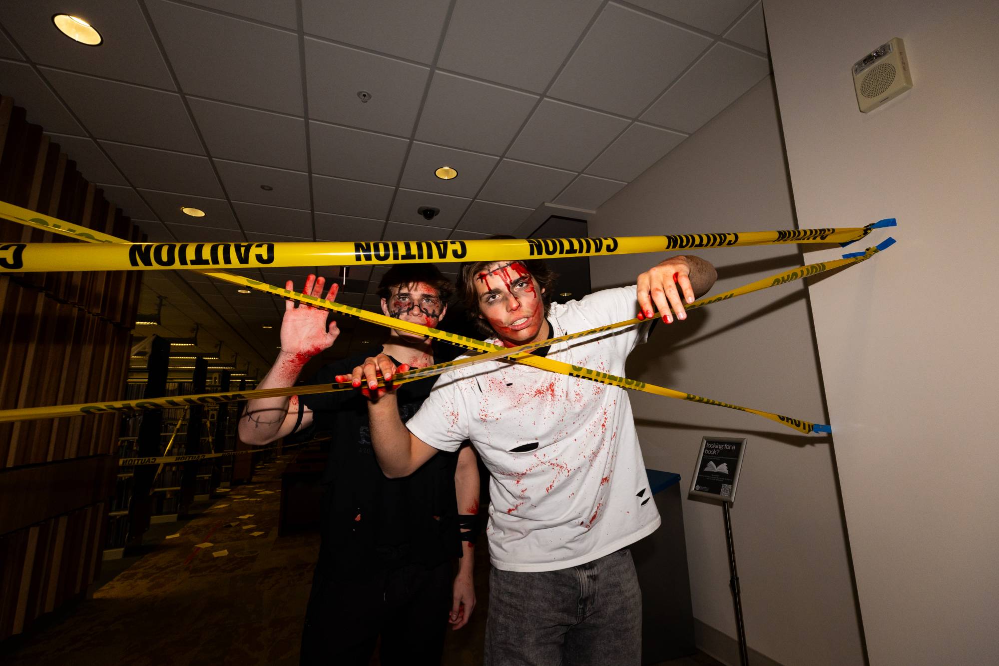 Two students dresses as zombies breaking through yellow caution tape